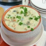 A bowl of creamy Instant Pot Chicken Gnocchi Soup garnished with fresh parsley, served on a white plate with stacked dishes in the background.