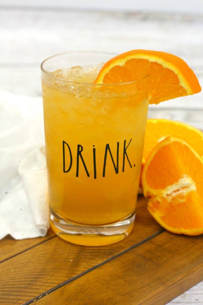 energy drink in a clear glass with a drink label on it, with a slice of orange in the drink and oranges next to it.