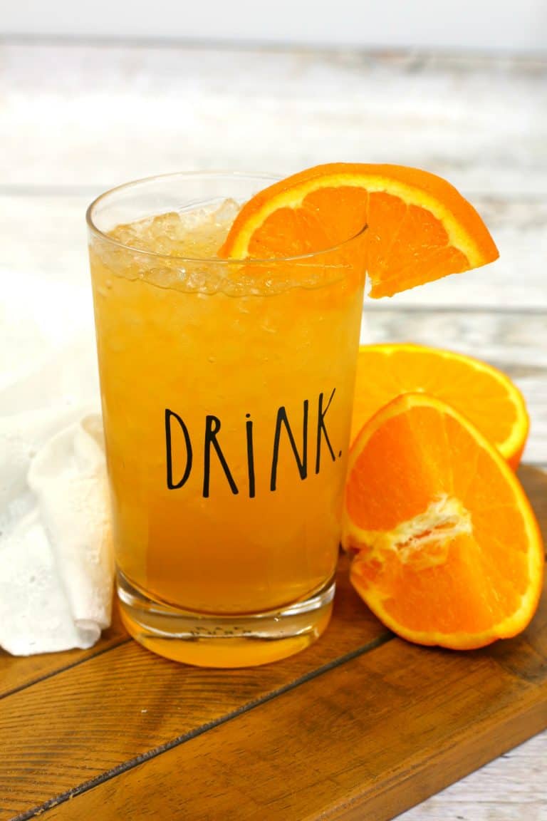 energy drink in a clear glass with a drink label on it, with a slice of orange in the drink and oranges next to it.