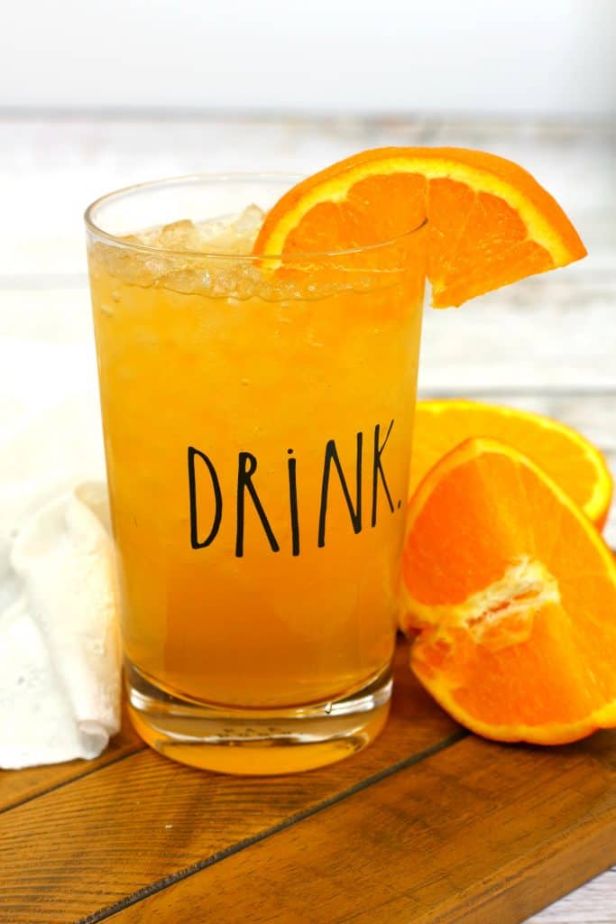 energy drink in a clear glass with a drink label on it, with a slice of orange in the drink and oranges next to it.