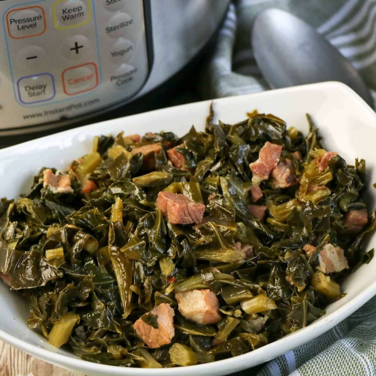 A bowl of Instant Pot Collard Greens with pieces of meat sits beside the cooker and a metal spoon.