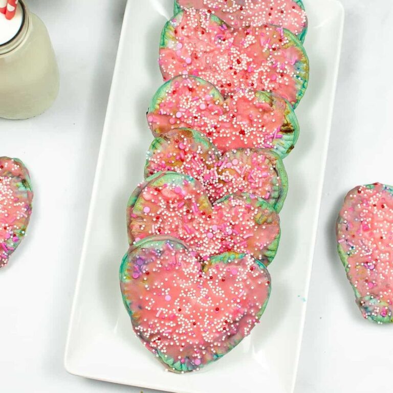 Heart-shaped cookies with pink icing and colorful sprinkles are arranged on a rectangular white plate, reminiscent of whimsical Air Fryer Unicorn Pop Tarts, with a bottle of milk nearby.