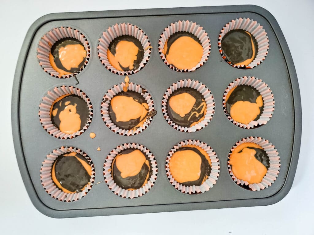 orange and black cake batter swirled into a muffin baking tin.