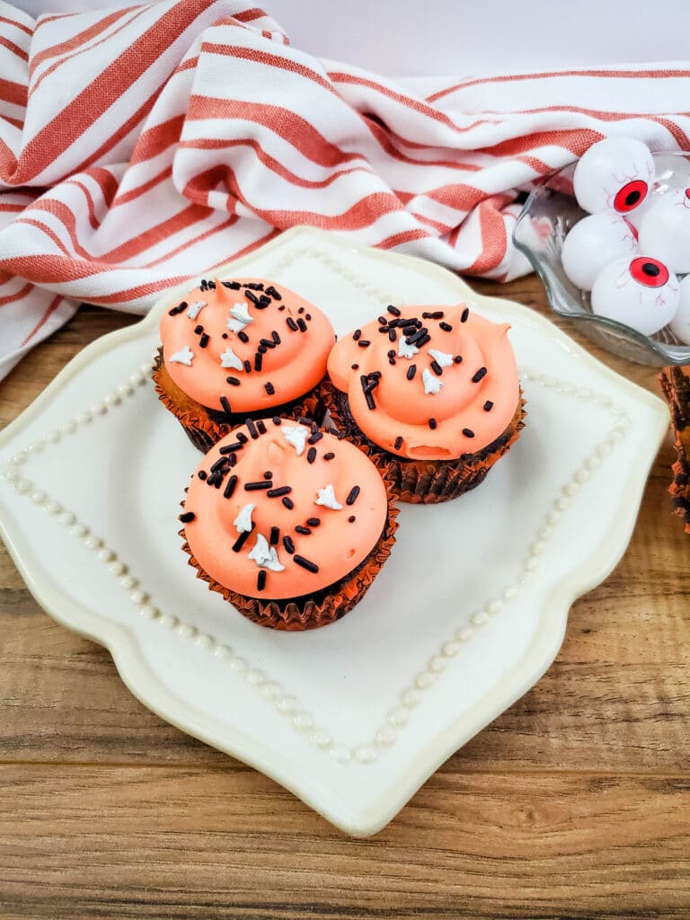 birds eye image of three halloween cupcakes with orange frosting and sprinkles on a white plate