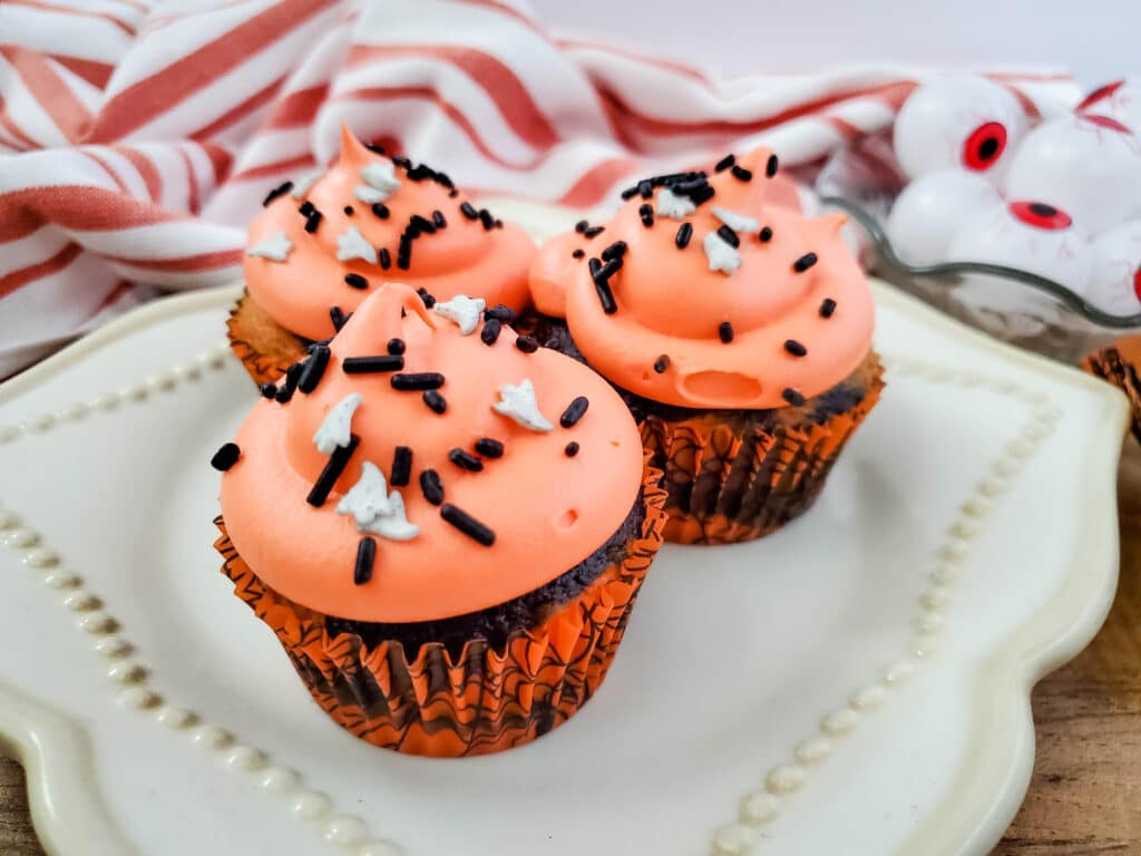 3 Halloween Tie Dye Cupcakes on a white plate with a bowl of plastic eyeballs in the background