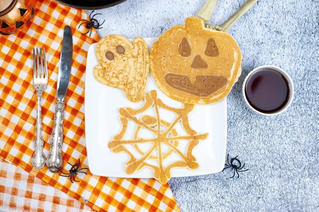 close up birds eye image of halloween pancakes on a white plate with syrup next to it.