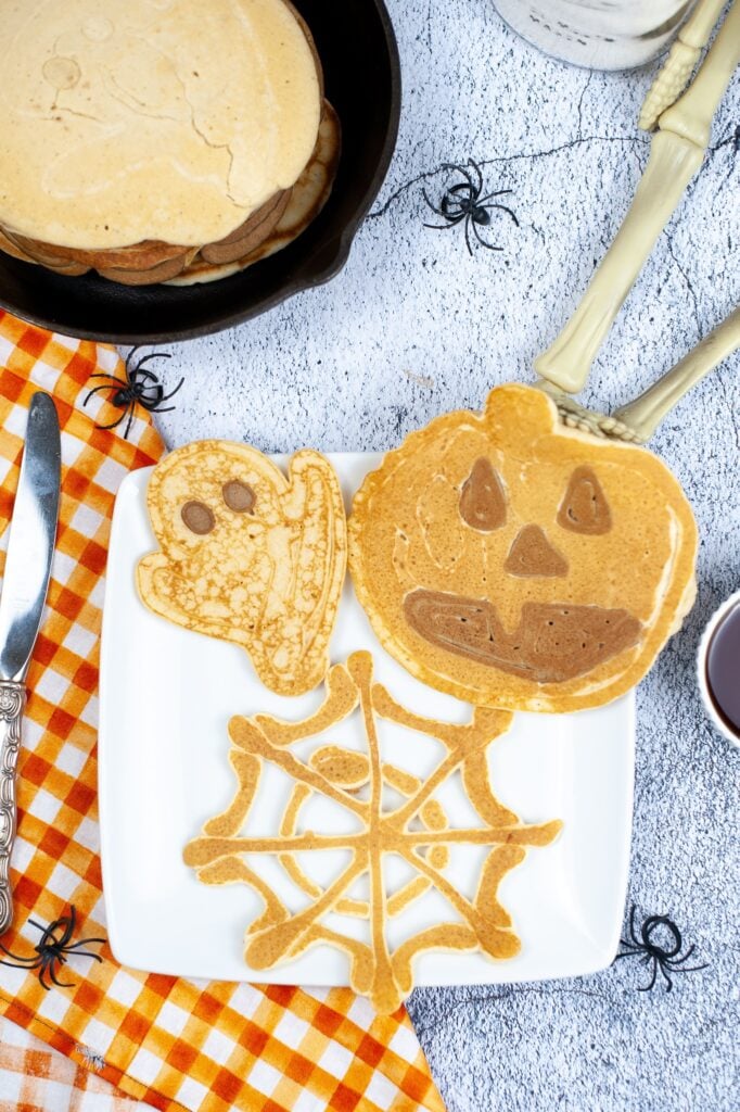 Birds Eye image of three halloween pancakes on a white plate with a burnt orange and white checkered napkin