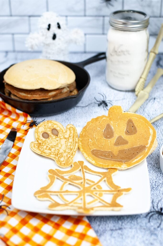 vertical image of jack o lantern pancake, ghost pancake and spider web pancake on a white plate