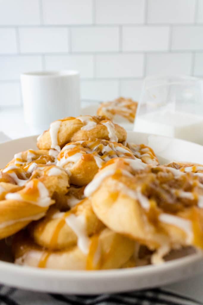 Close up of a plate full of caramel apple danishes with a cup of coffee in the background