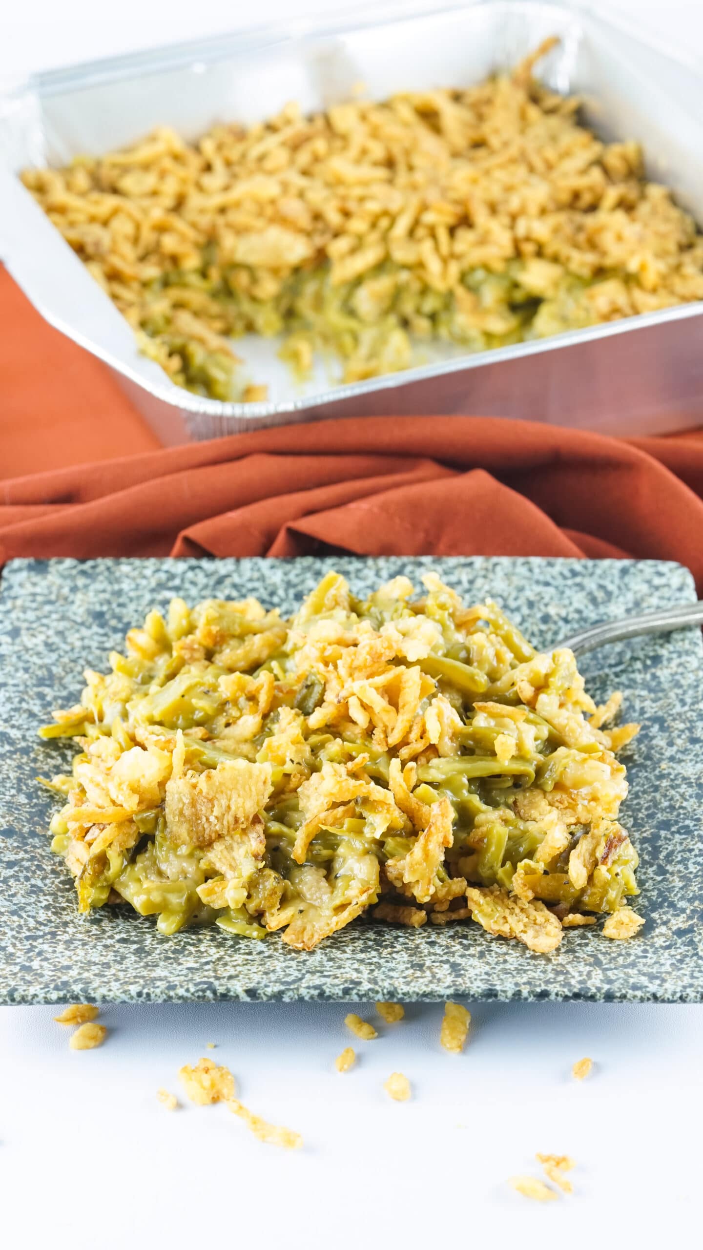 Side view angle of smoked green bean casserole on a black and white marble plate with the pan of casserole in the background.