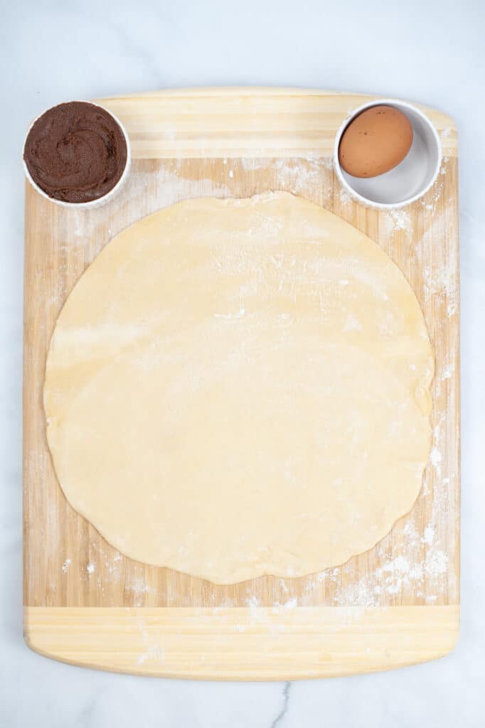 pie crust rolled out on a cutting board with a bowl of nutella and an egg
