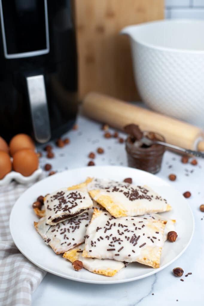 Birds Eye Image of six finished nutella poptarts on a white plate with an air fryer in the background.