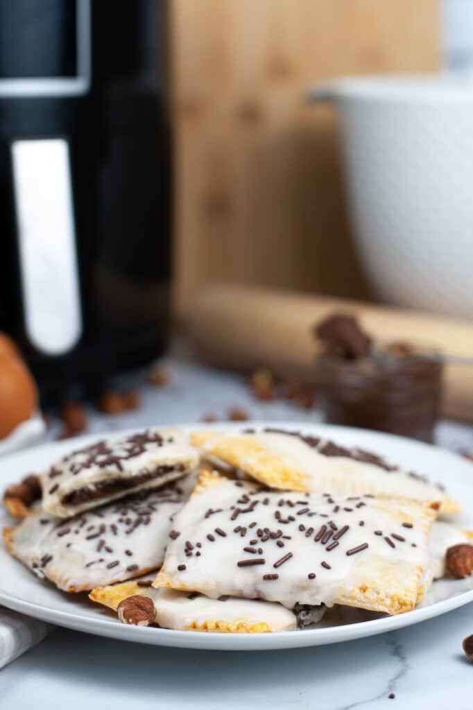 veritcal image of a plate with 12 nutella poptarts and an air fryer in the background.