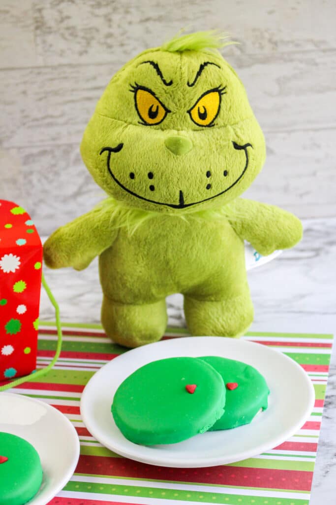 Grinch Cookies on a white plate with a stuffed grinch in the background
