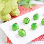grinch oreo balls on a white platter with a stuffed grinch in the background