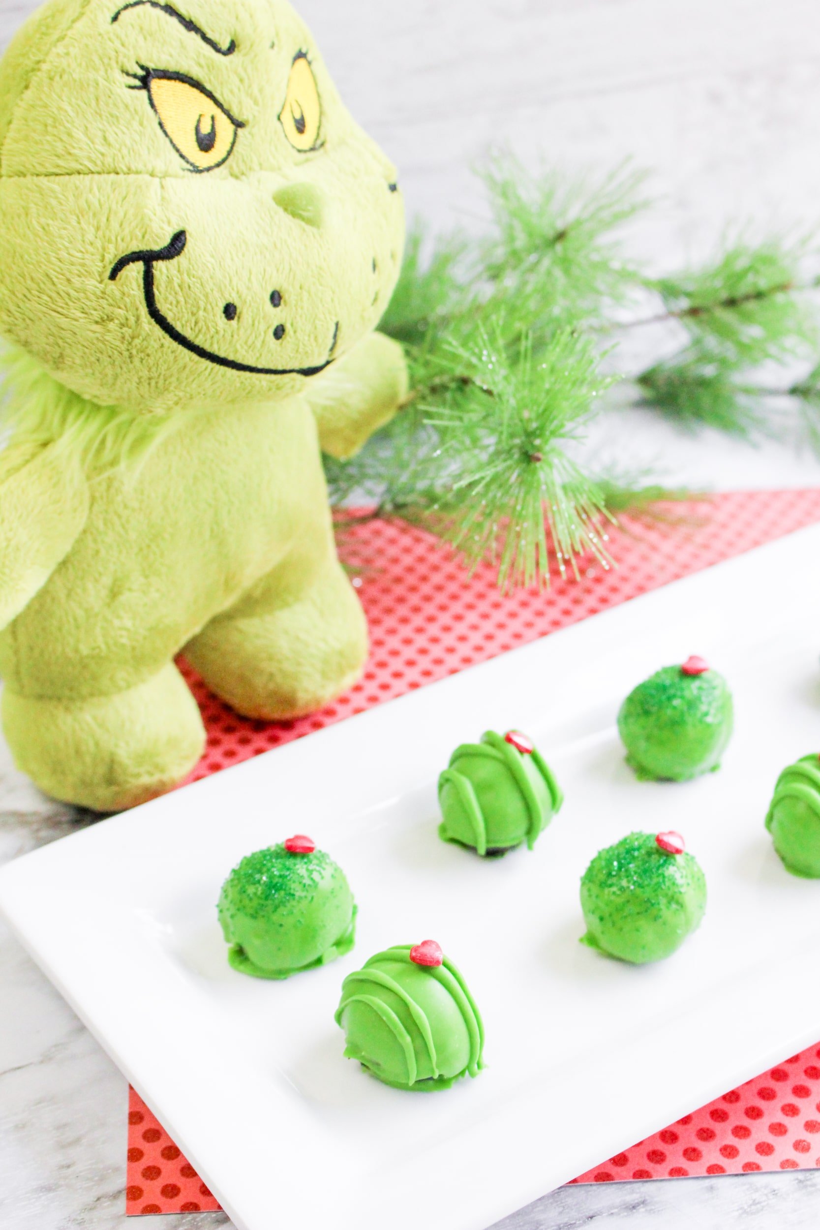 Grinch Oreo Balls on a white platter with a stuffed grinch in the background