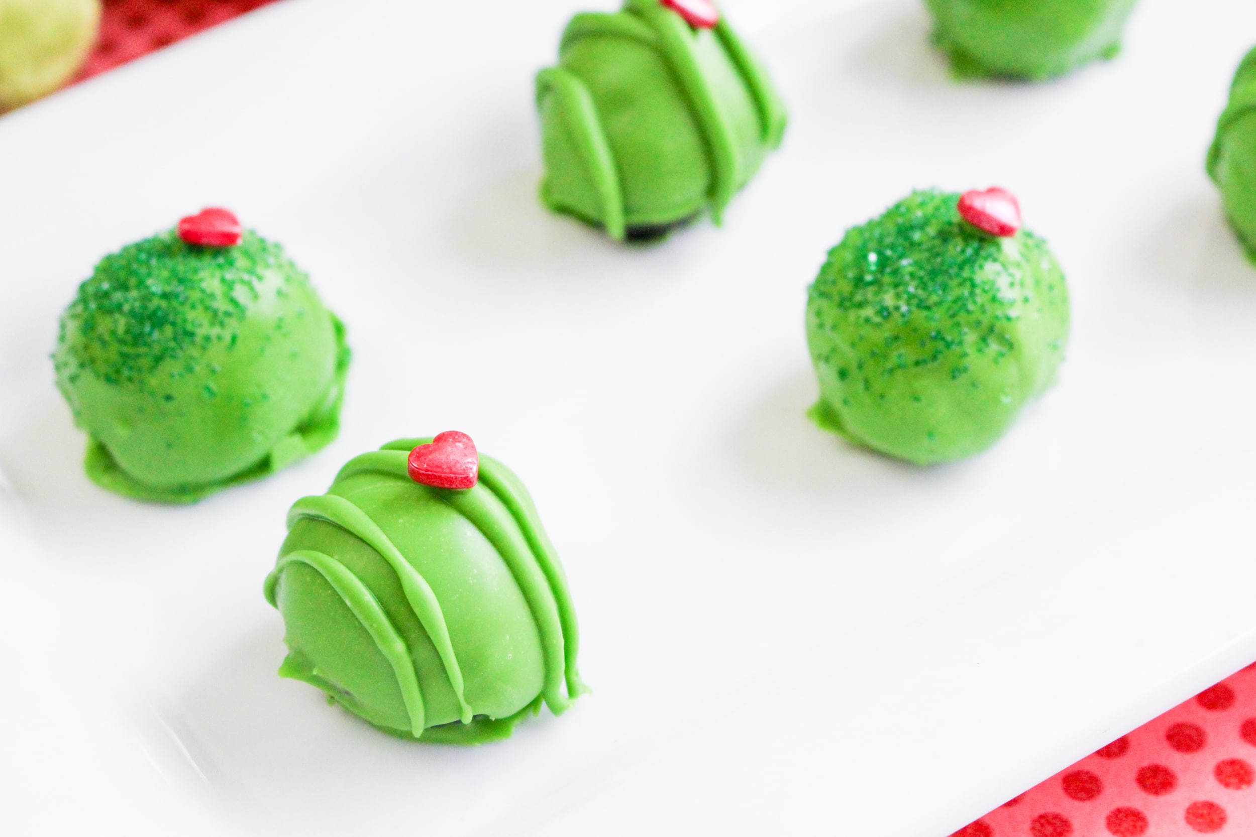 close up image of six grinch oreo truffles on a white serving platter with a red table cloth