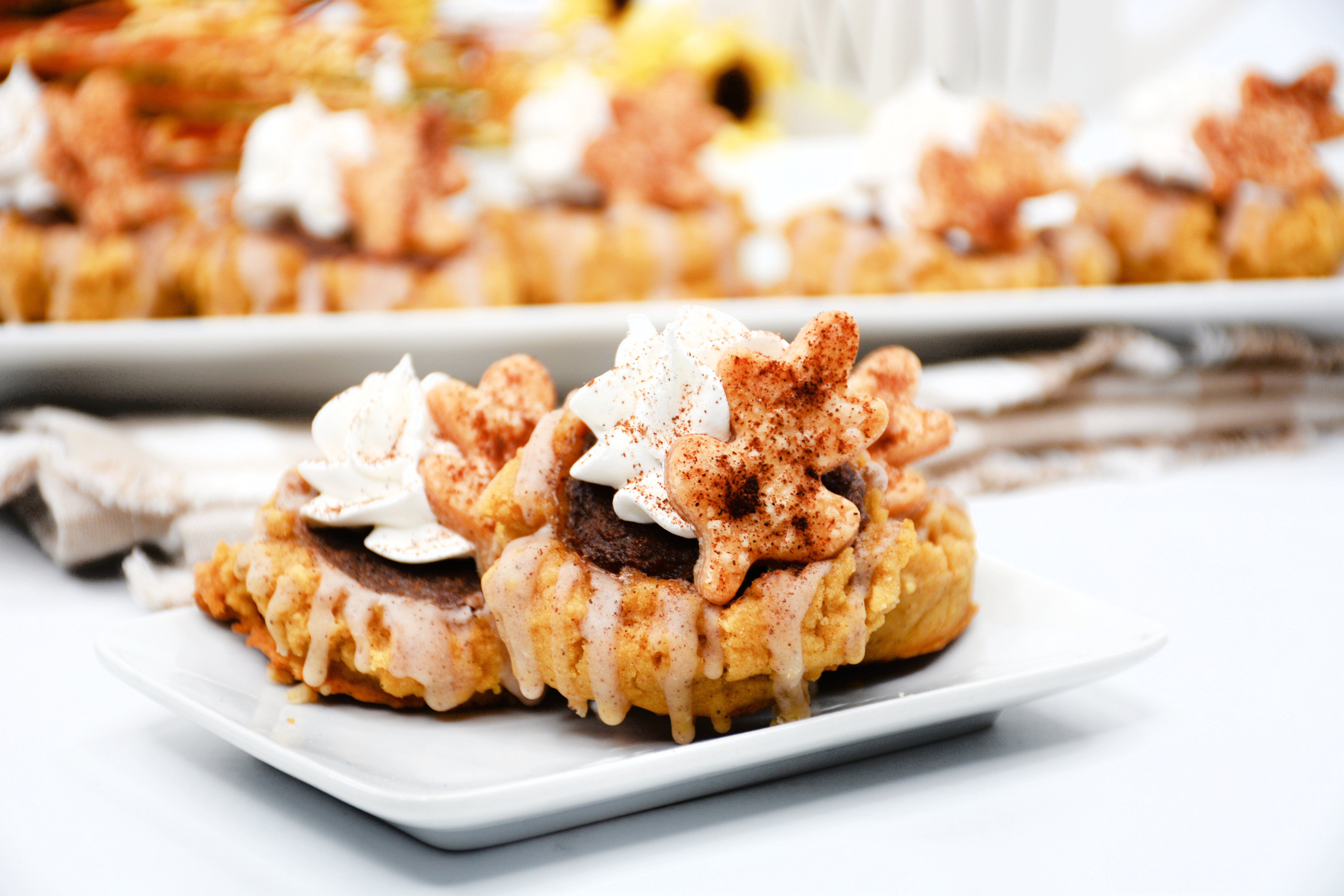 horizontal image of three pumpkin cookies that are topped and glazed on a white plate.