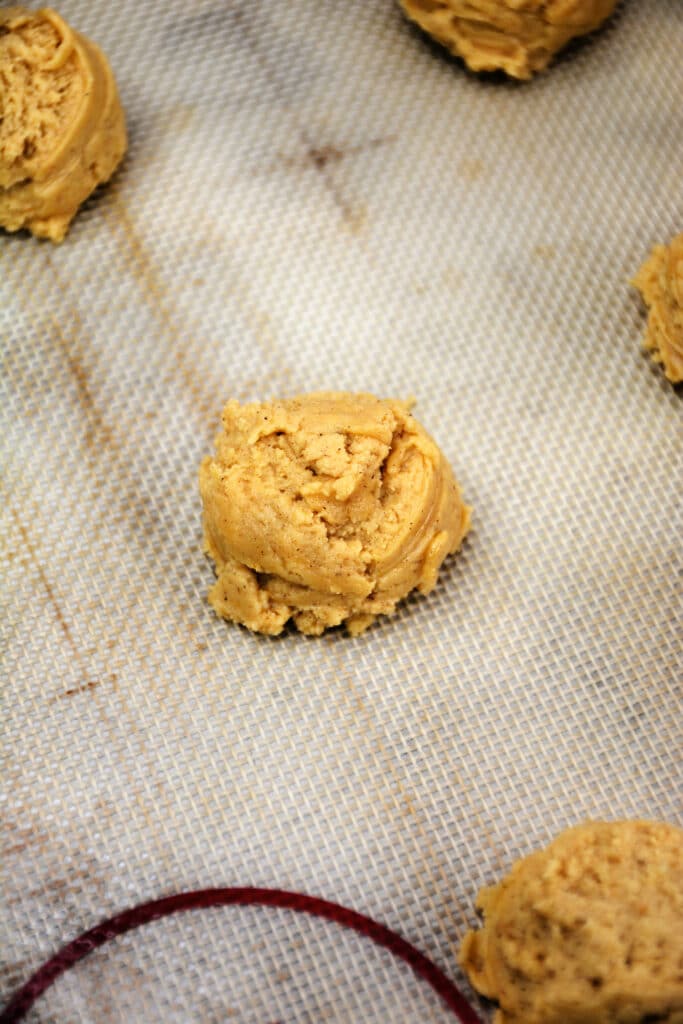 scoops of pumpkin cookie dough on a baking sheet lined with a baking mat