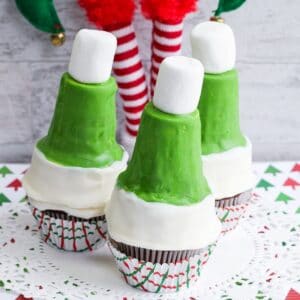 image of three green elf hat cupcakes with a stuffed upside elf behind them