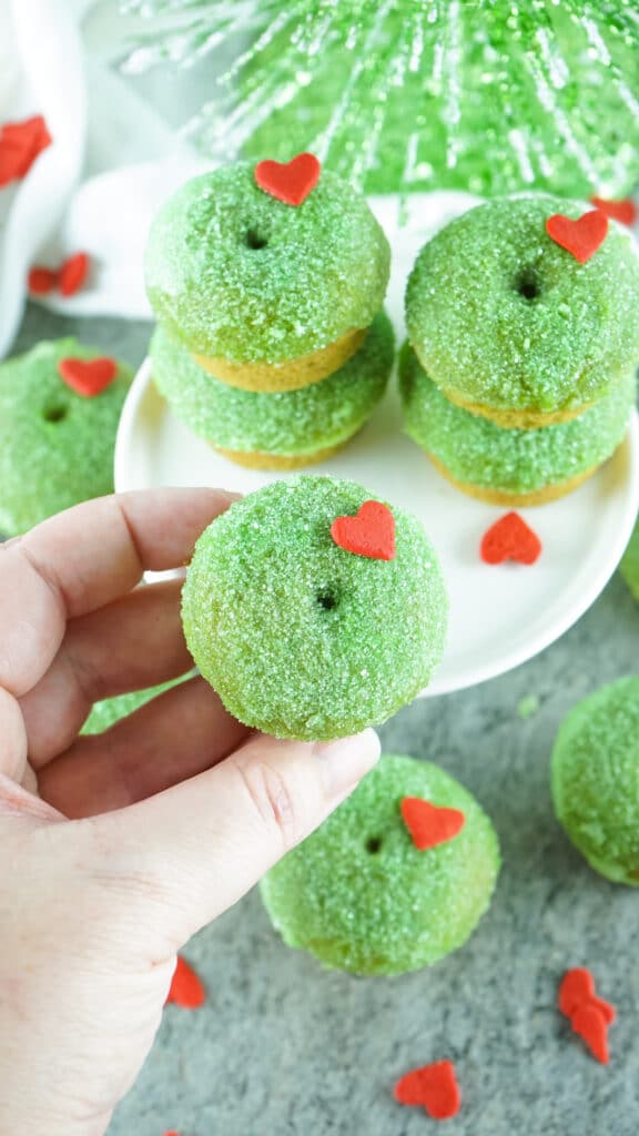 Grinch Donuts on a white cake stand with a bottle tree in the background