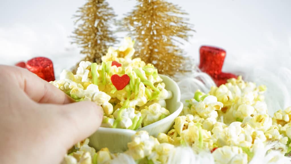 close up image of a bowl of grinch popcorn with a womans hand