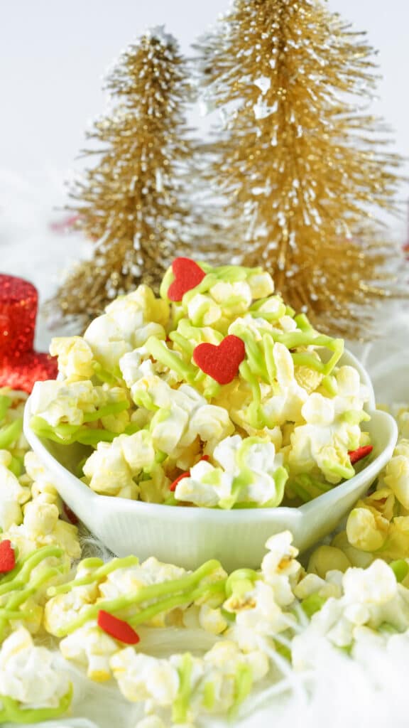 white bowl filled with grinch popcorn with christmas trees in the background
