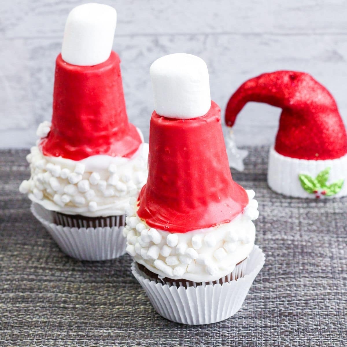 square image of two santa hat cupcakes on a gray placemat