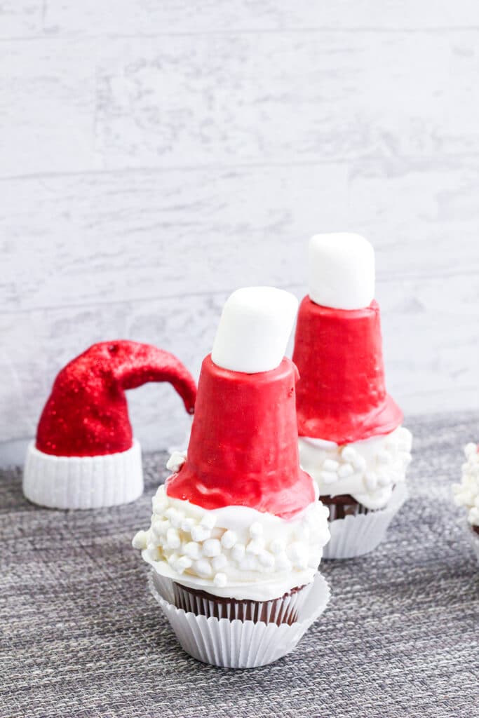 Two Santa Hat Cupcakes on a table with a plastic santa hat in the background