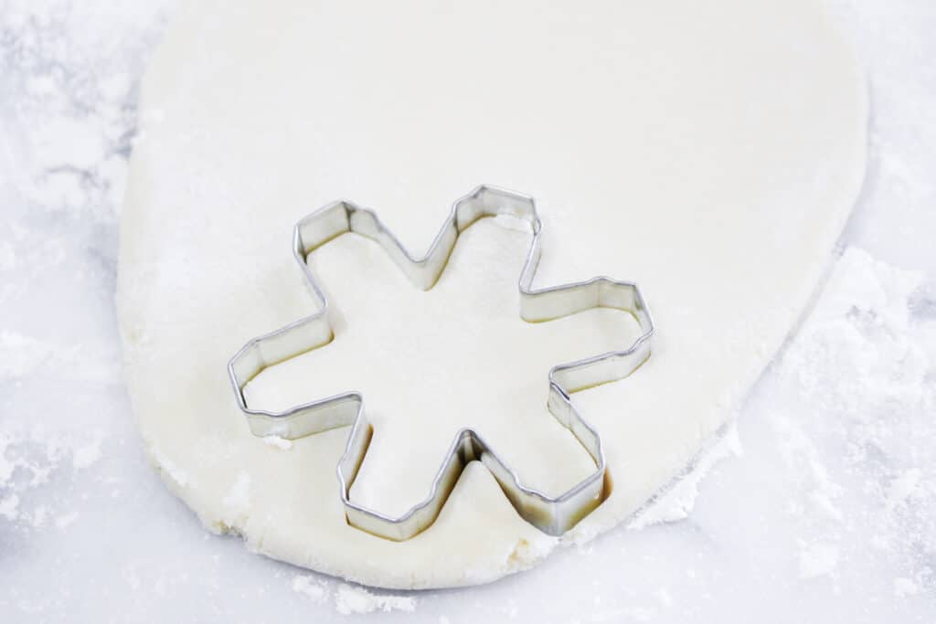 snowflake cookie being cut out of rolled cookie dough.