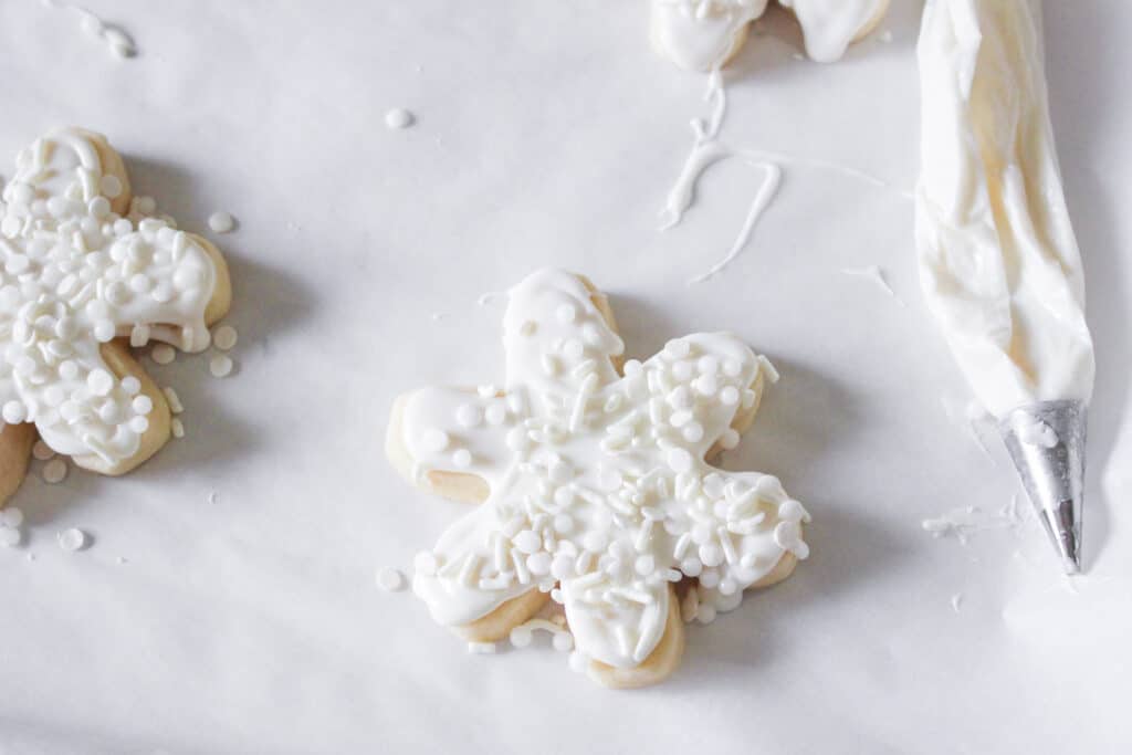snowflake shaped cookie being frosted and sprinkled
