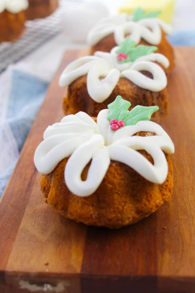 vertical image of a three mini christmas bundt cakes in a line on a wooden cutting board