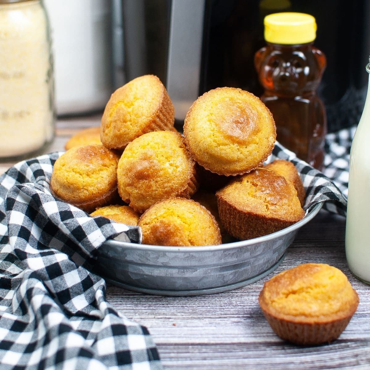 square image of air fryer cornbread muffins with a bottle of honey behind it.