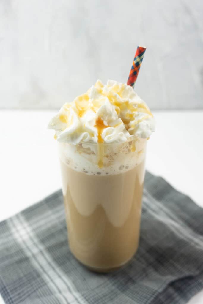 Vertical image of Caramel Brulee Latte in a tall glass with a red straw on a gray napkin