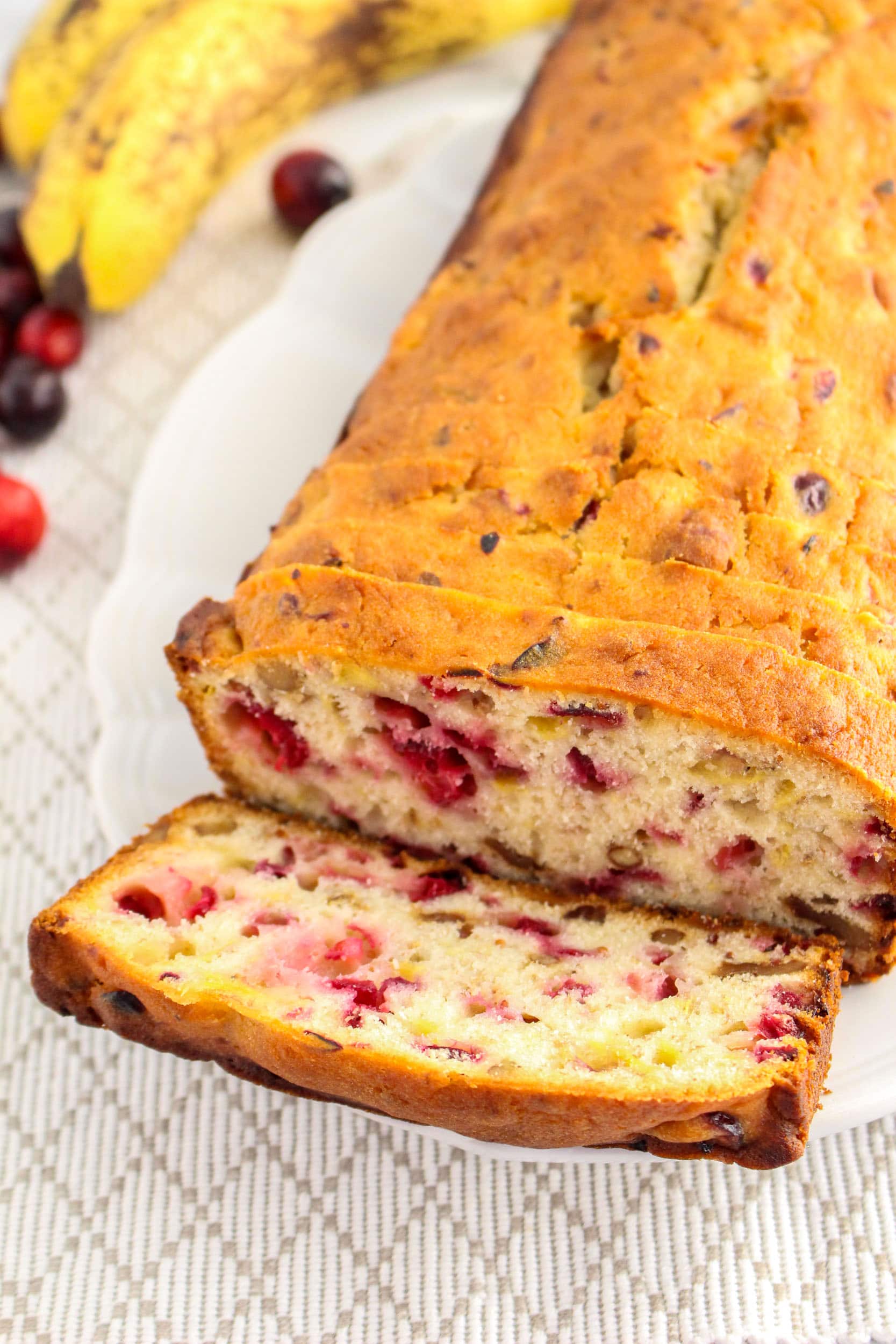 vertical image of a Loaf of Cranberry Banana Bread on a white plate