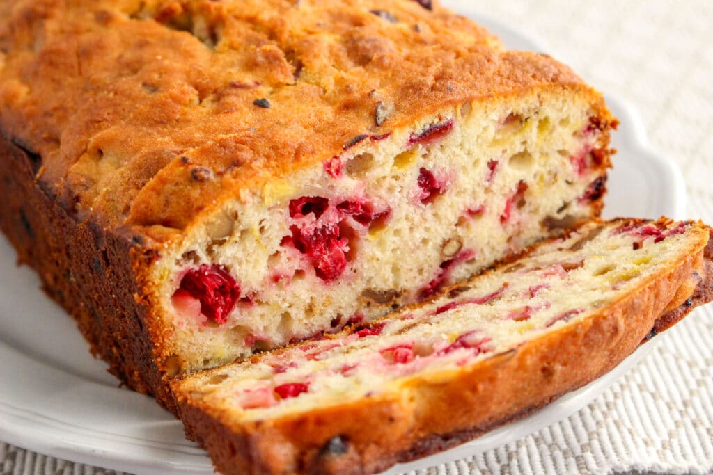 side view of a Loaf of Cranberry Banana Bread on a scalloped white plate