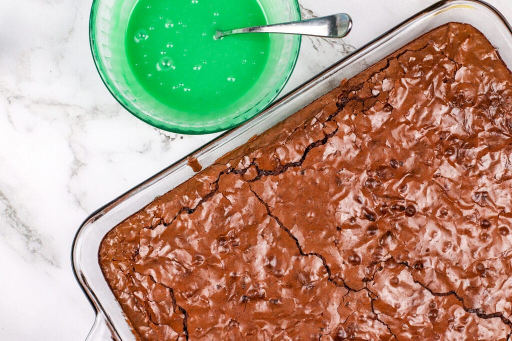 baked brownies next to a bowl of green frositng