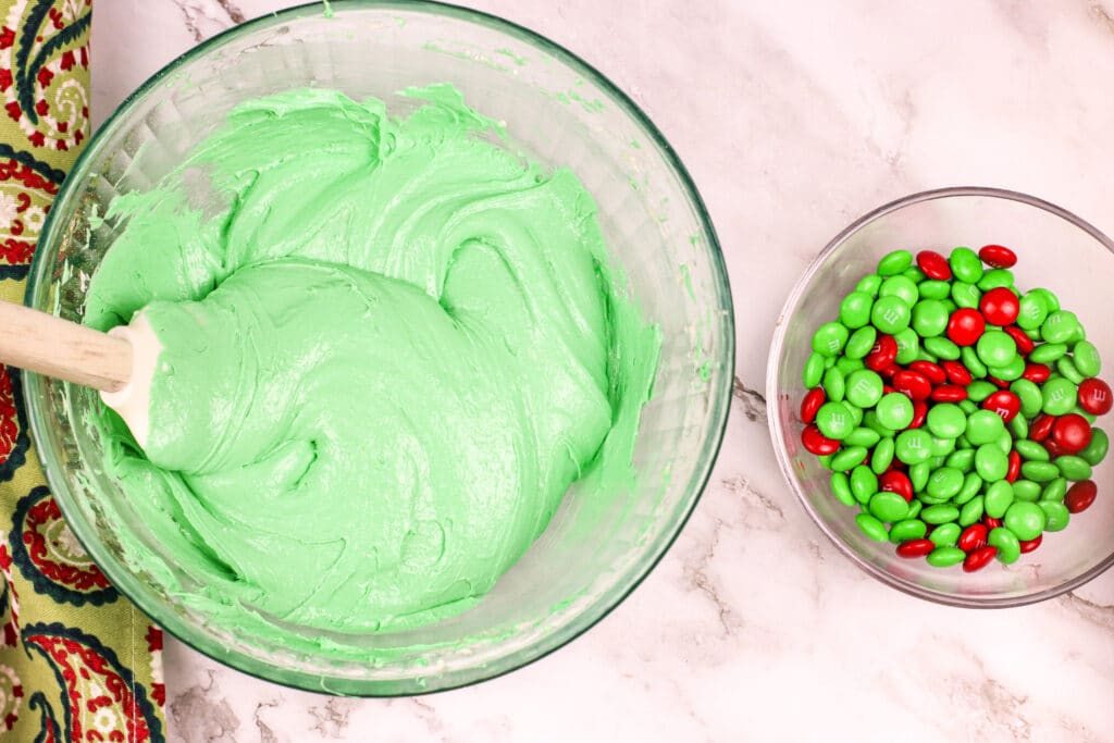 green cake mix in a glass mixing bowl with a small bowl of M&M candies