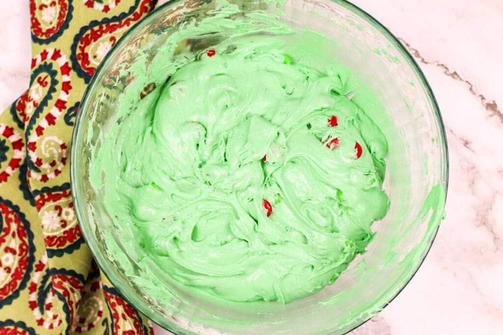 green cookie dough in a glass mixing bowl with green Mms