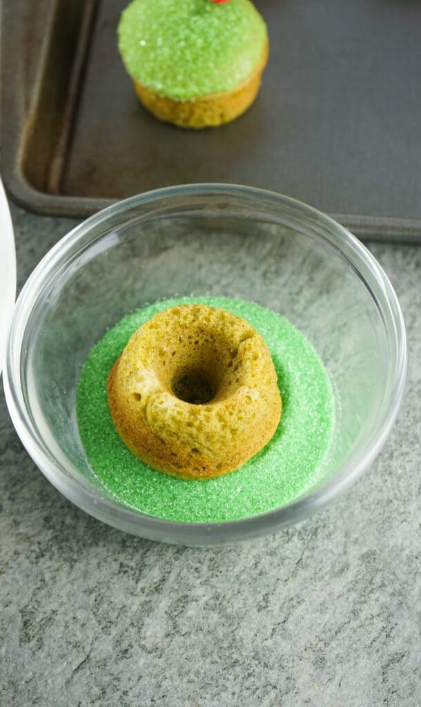 baked donut being dipped in green sanding sugar