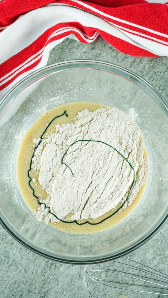 flour and eggs in a glass mixing bowl with a squirt of green food coloring