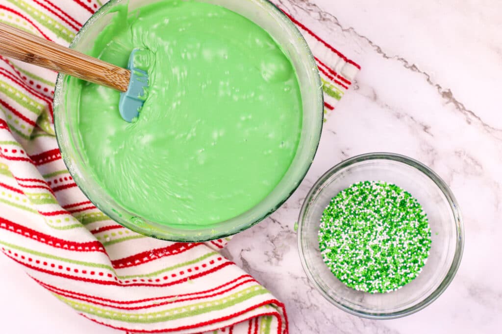 green fudge in a glass mixing bowl with a small glass bowl full of green and white sprinkles