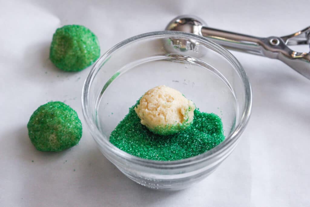 cookie dough ball in a small bowl of green mixing sugar