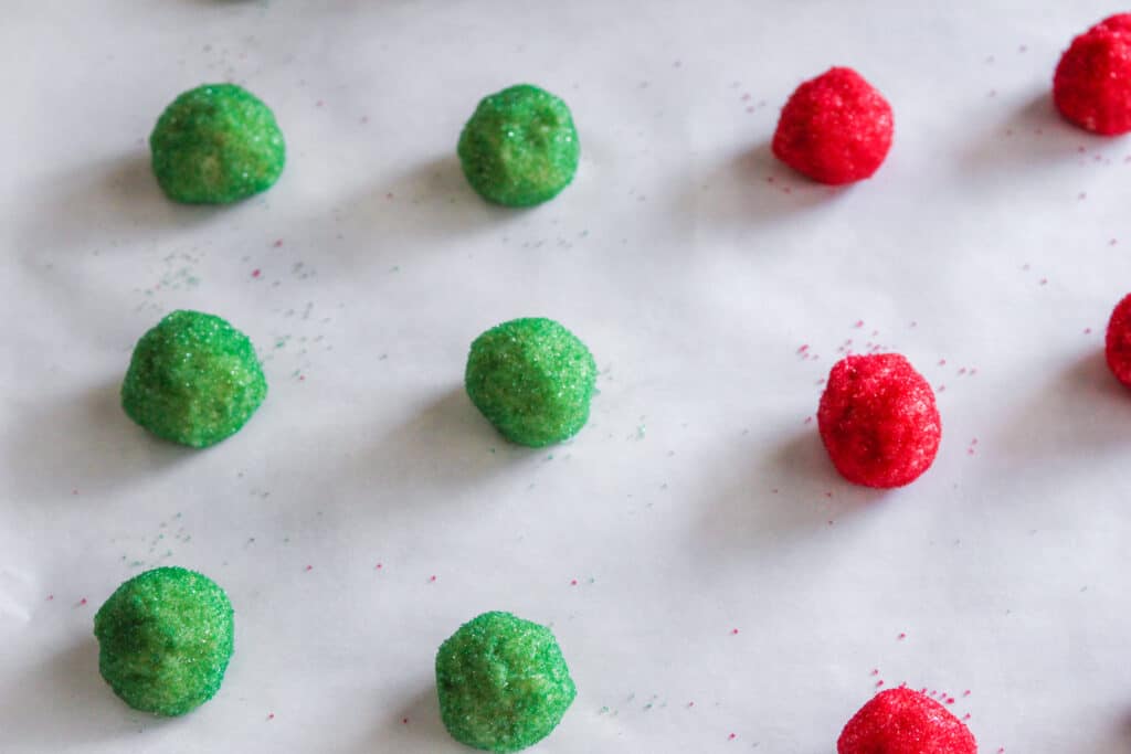 red and green sugar cookie balls on a parchment lined baking sheet
