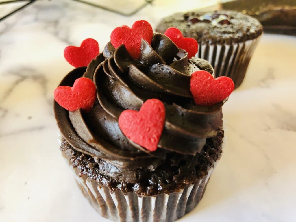 chocolate cupcake frosted with red heart sprinkles on it