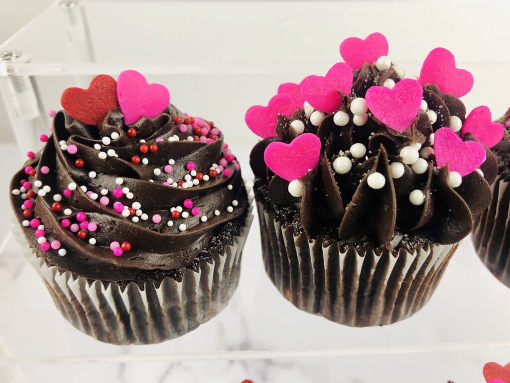 close up image of two Dark Chocolate Raspberry Cupcakes on a clear glass cupcake stand