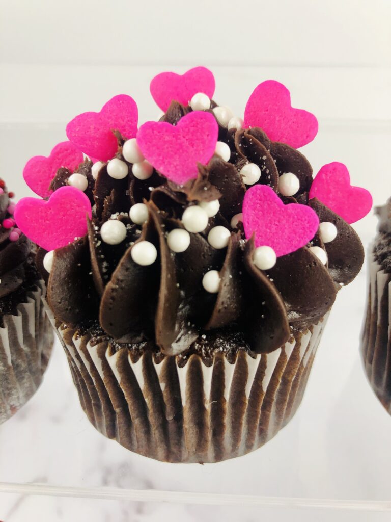 chocolate cupcake topped with pink hearts and white ball sprinkles