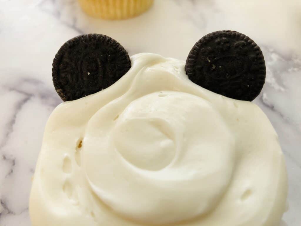 mini oreos on top of a cupcake frosted with white frosting