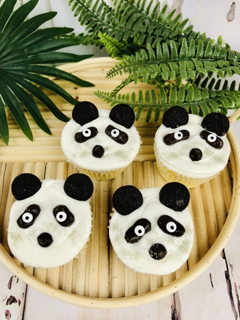 Vertical image of four panda cupcakes on a bamboo serving tray