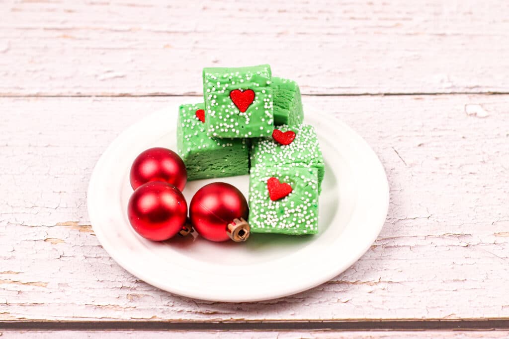 Grinch Fudge on a small white plate with small red ornaments next to the fudge